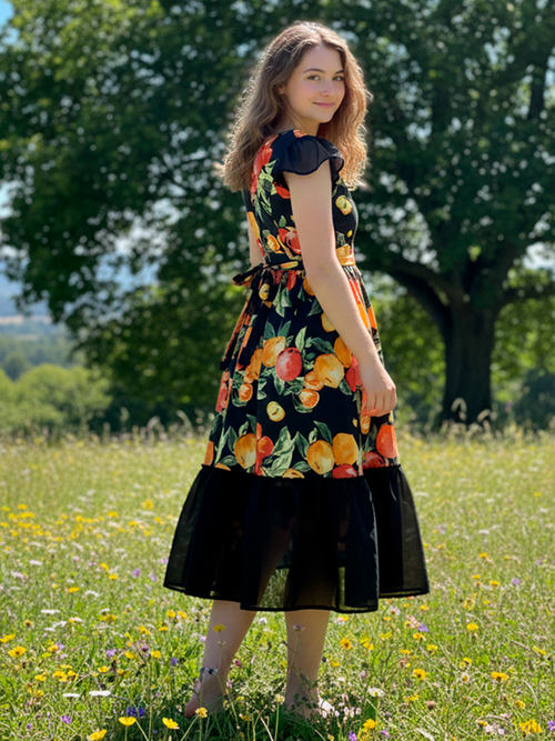 Woman in a floral dress standing in a field with trees in the background
